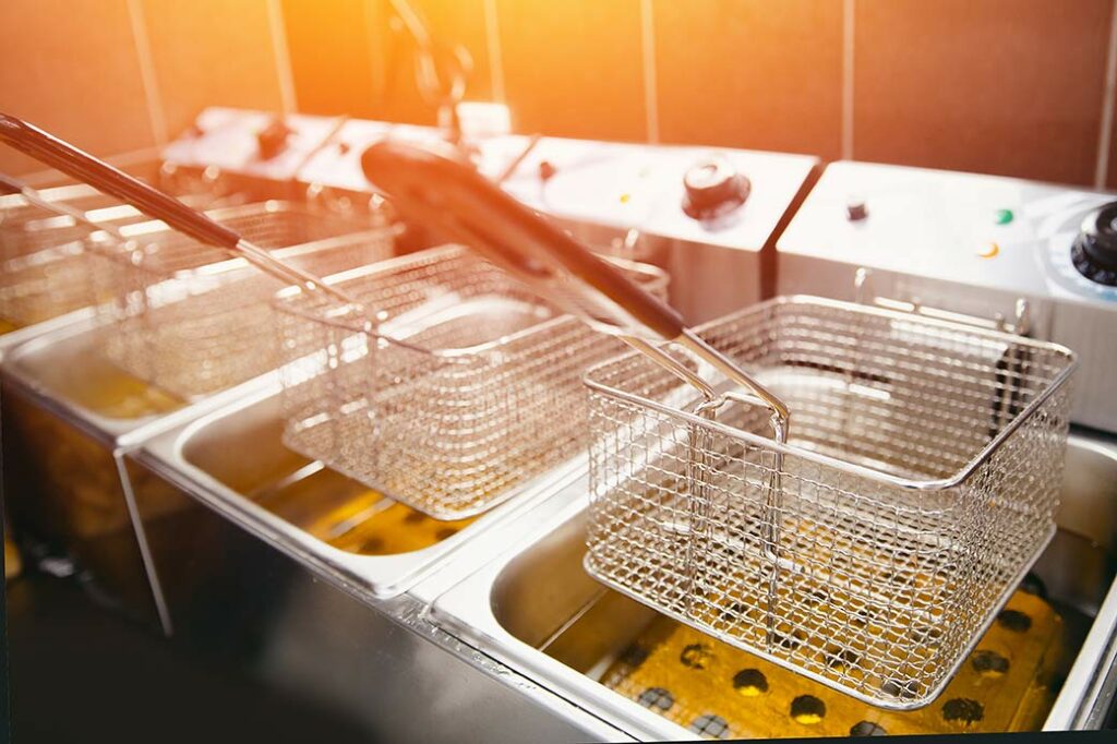 Bank of four deep friers with baskets empty and clean, and raised over oil-filled basins. 