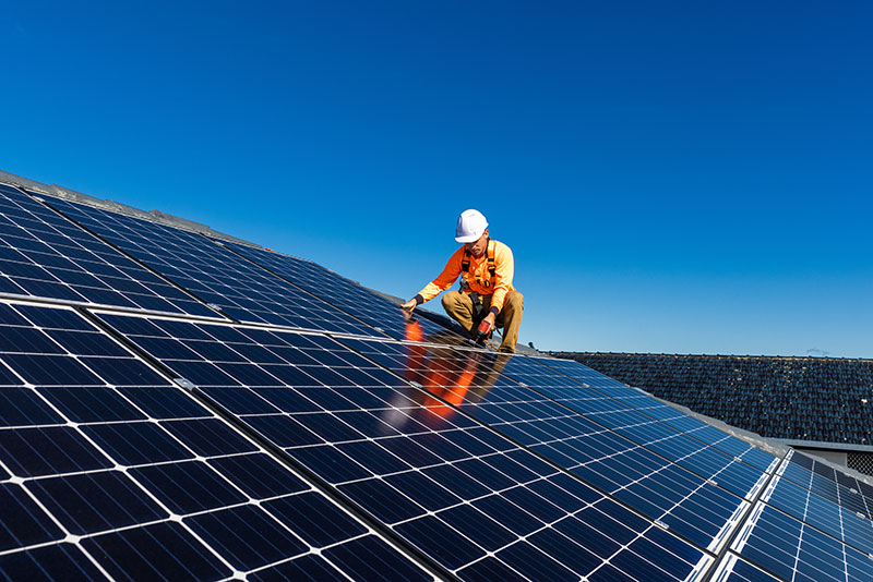 man wearing work clothes and hard hat installing solar panels on a cloudless day