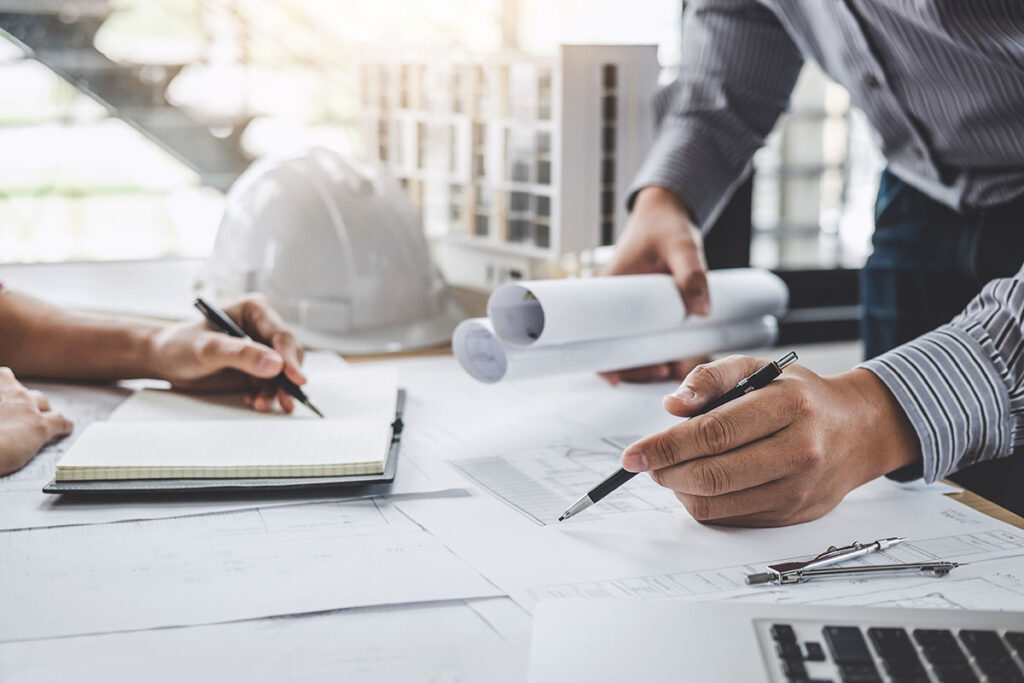 Two people stand over a white desk covered in papers, planning during the pre-construction phase of a winery remodel project to ensure time efficiency.