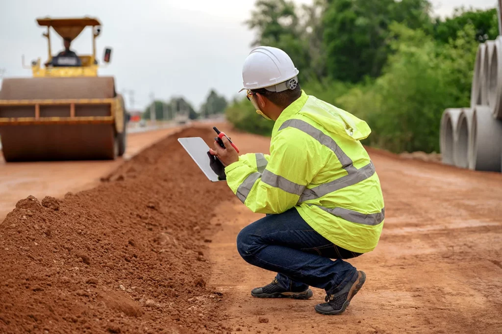 An engineer in a bright yellow shirt and a white hard hat conducts soil analysis for a commercial construction project.