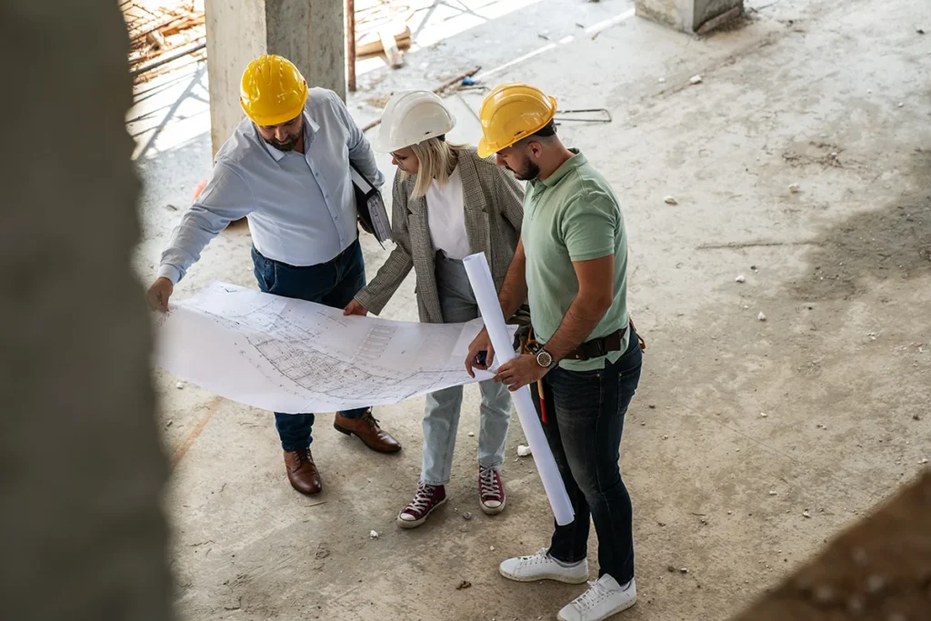 A commercial construction crew wearing hard hats, going over project plans with a general contractor