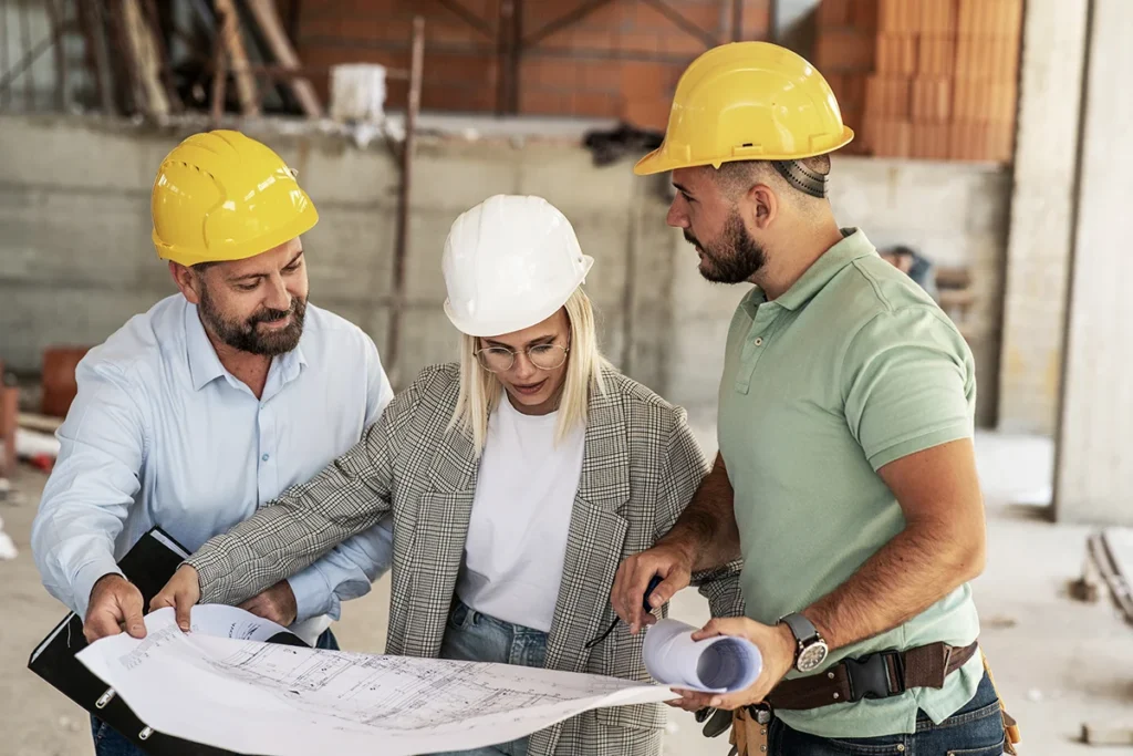 A general contractor stands with a design build team, going over construction plans in hard hats, showing the concept of the benefits of involving a general contractor in the design phase