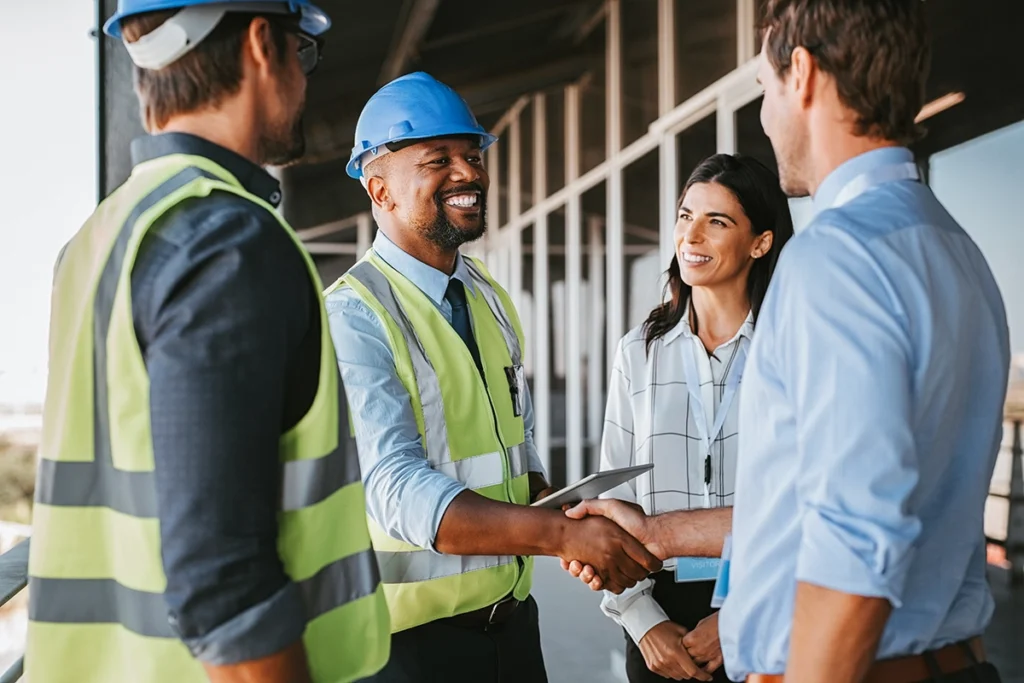 A smiling general contractor wearing a hard hat, shaking hands with clients